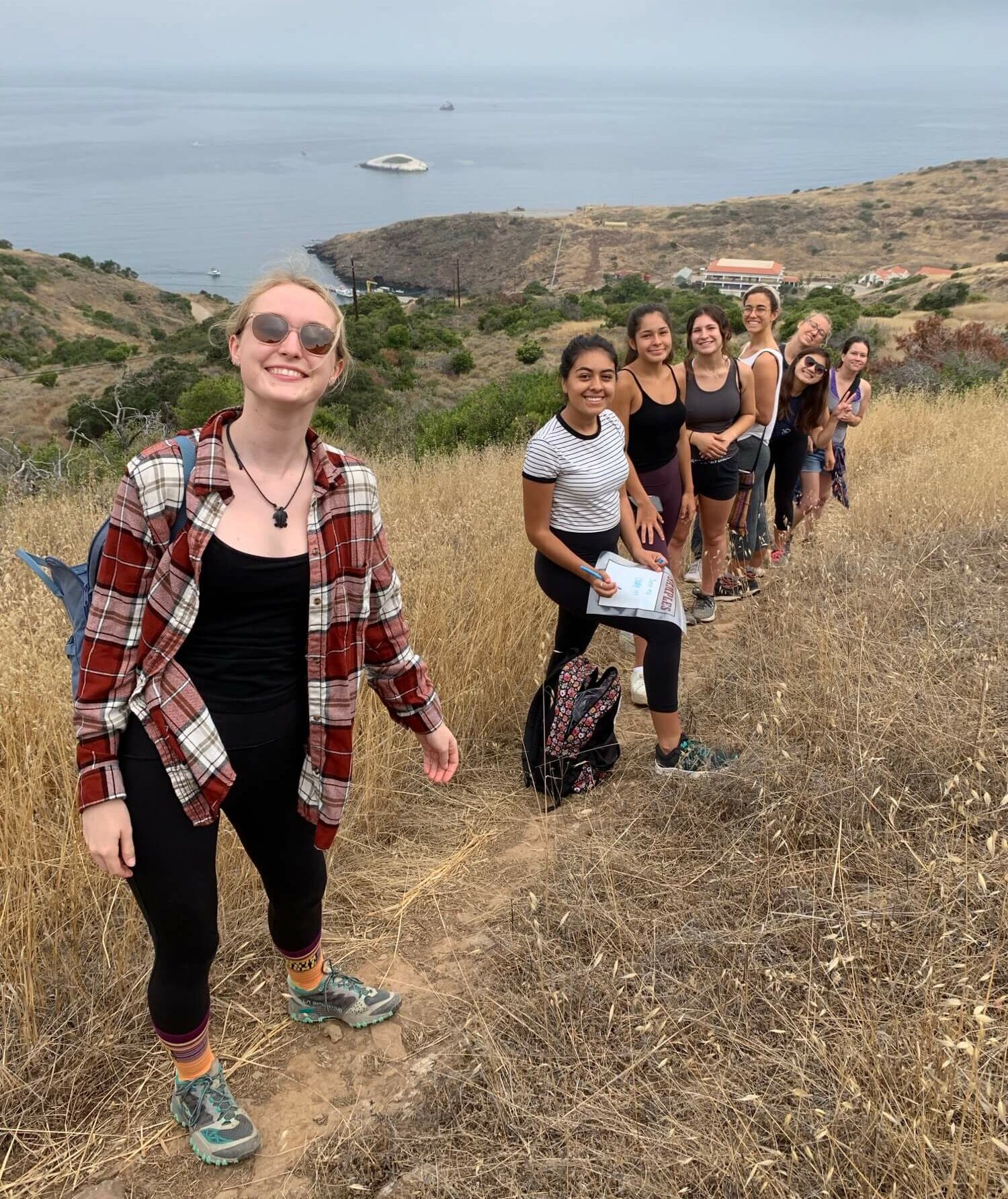 a line of Environmental Studies students stands in a field on a Catalina Island hillside with the ocean in the background