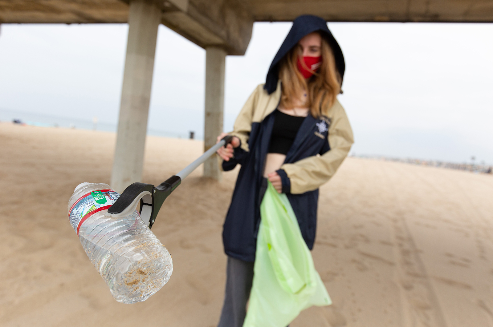 a student holds a trash bag and empty plastic water bottle collected from the beach at a cleanup event