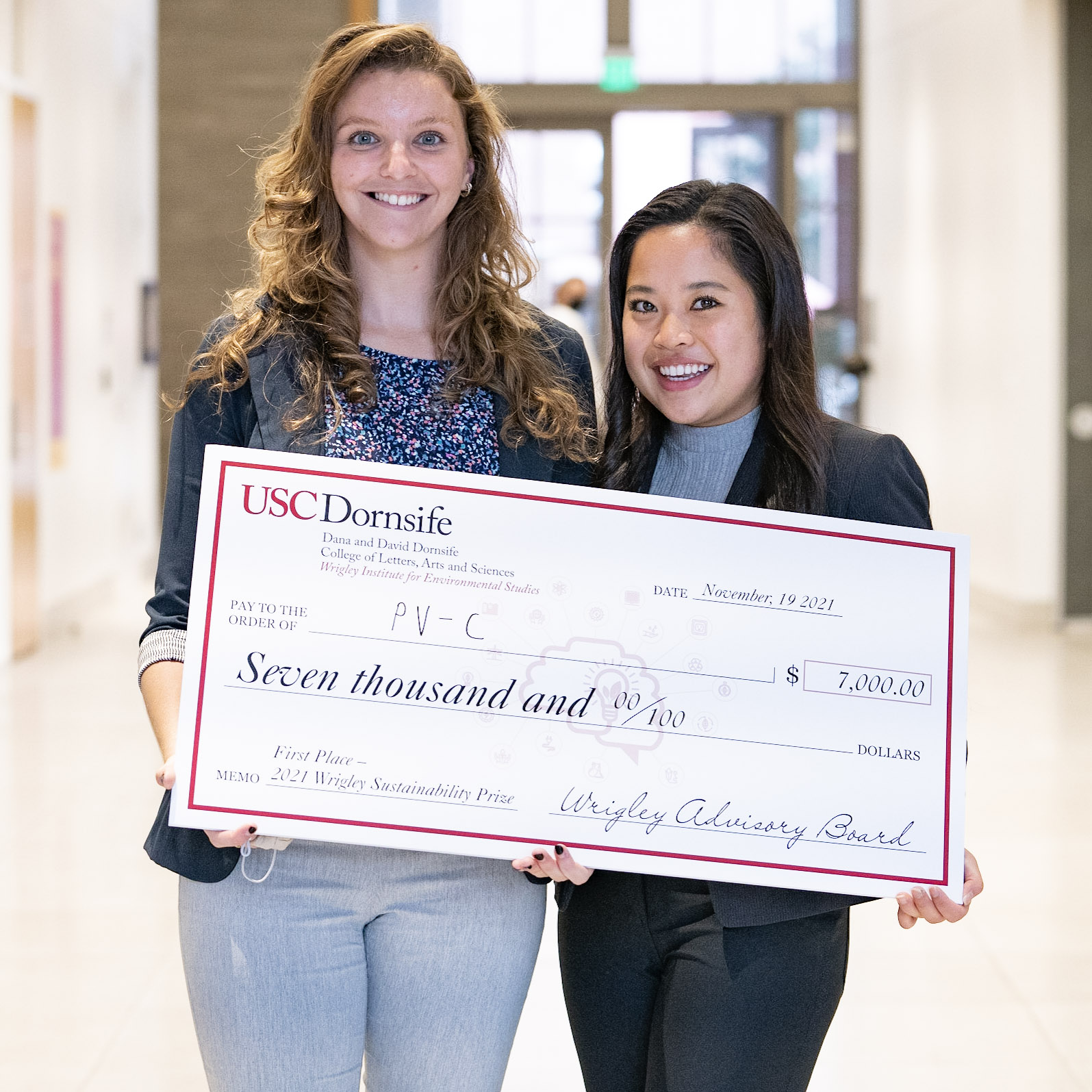 students Nancy Bush and Caitlin Dinh, wearing business suits, hold an oversize check representing their first-place winnings of $7,000 in the Wrigley Sustainability Prize competition for market-ready sustainable products or processes
