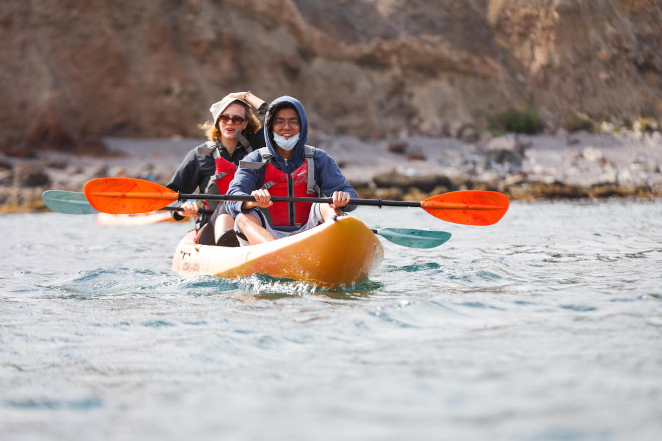 students smile and hold paddles across their laps as they float in a kayak off the Catalina Island coast
