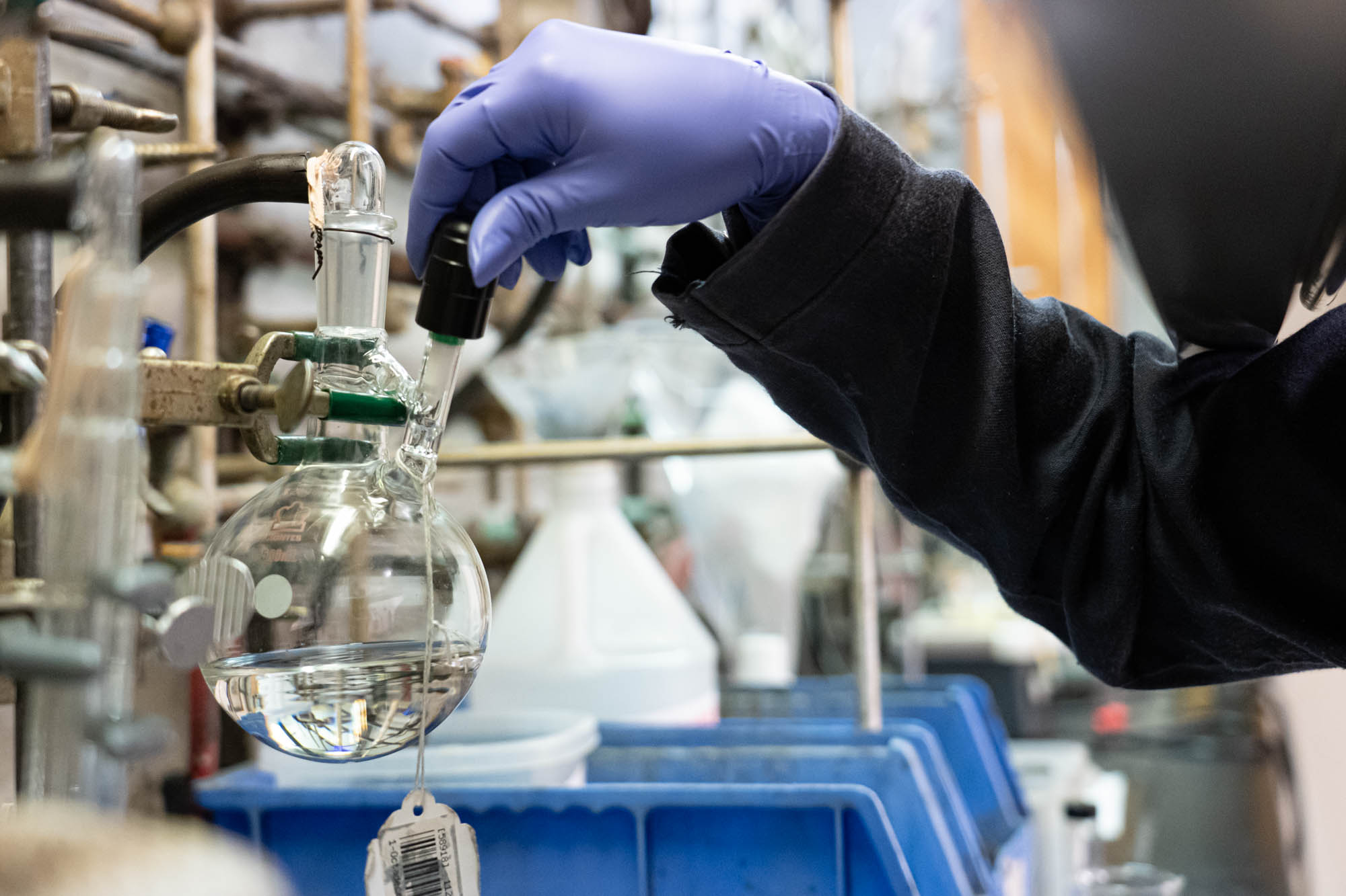 student wearing blue gloves with hand on a flask inside of a science lab