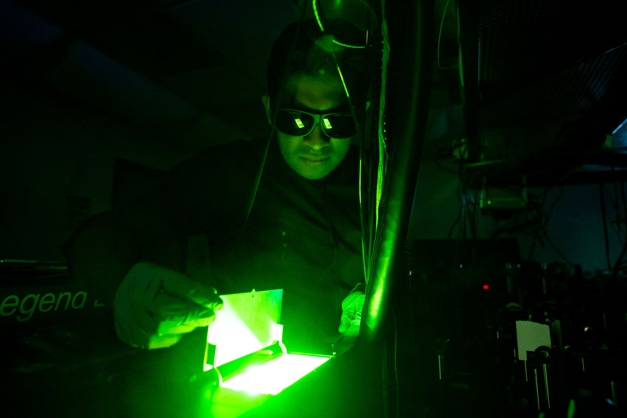 a graduate student wearing dark safety glasses looks into a container illuminated by a green laser