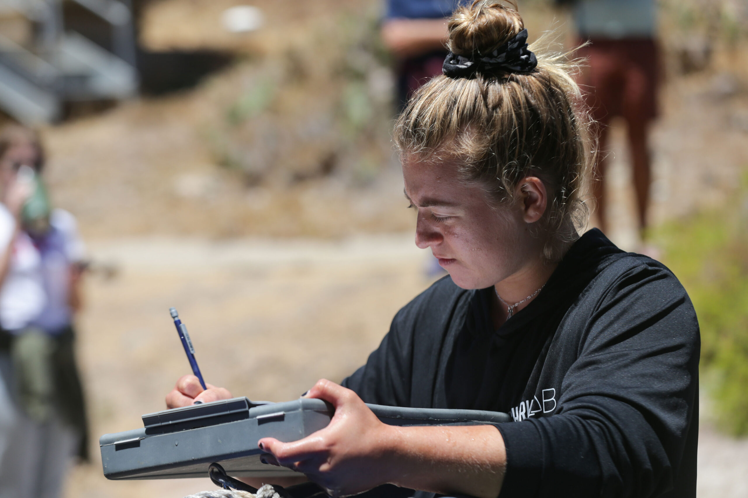 a person wearing a black shirt takes notes on a boxy metal clipboard