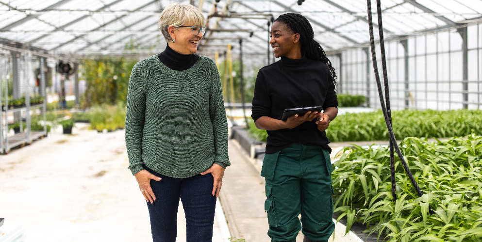 two sustainability professionals smile and talk to each other as they walk through a large greenhouse