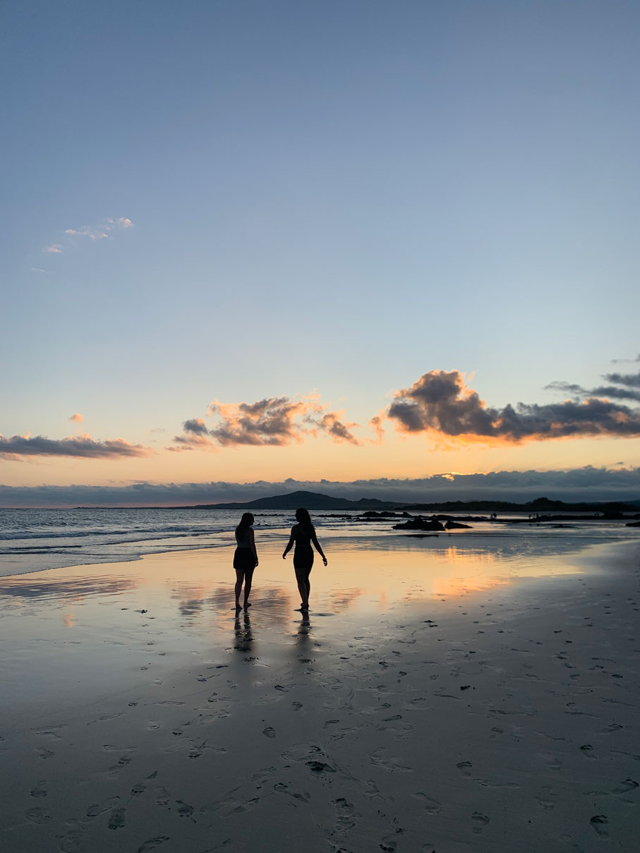 two friends walk on a beach at sunset