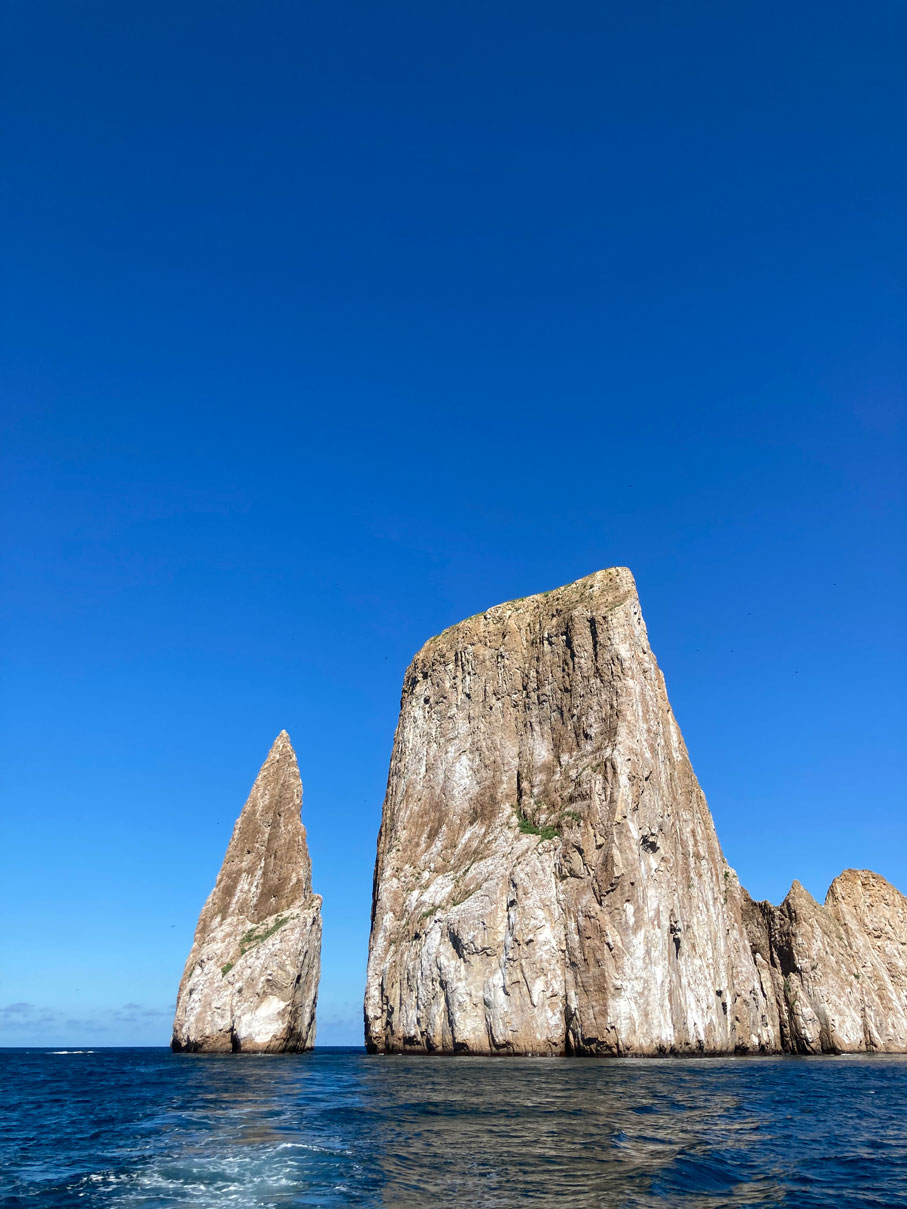 a large pillar of rock stands in the ocean, separated by a small expanse of water from another, larger rock pillar