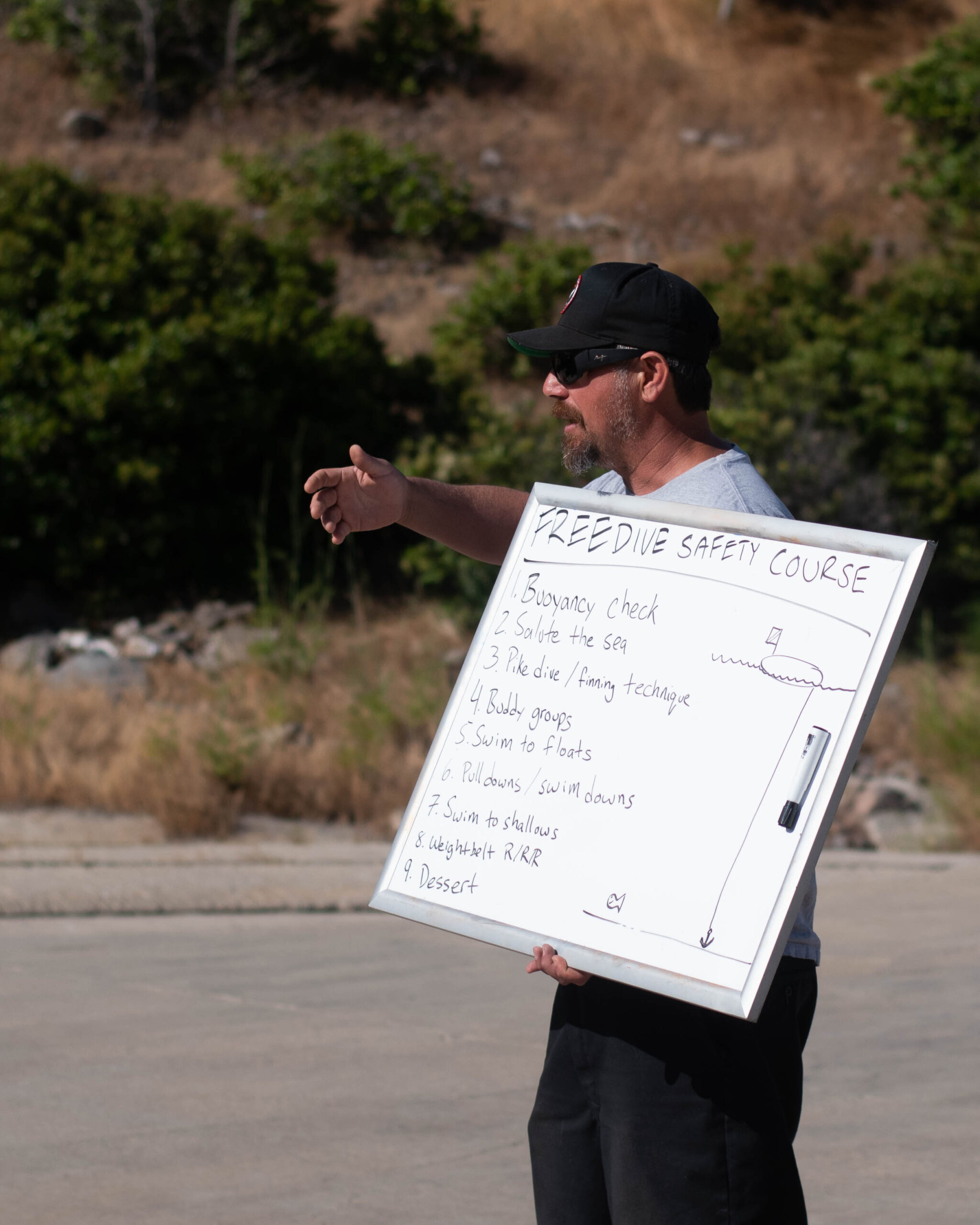 a man holds a large whiteboard with freediving instructions on it as he teaches a freediving course in the field