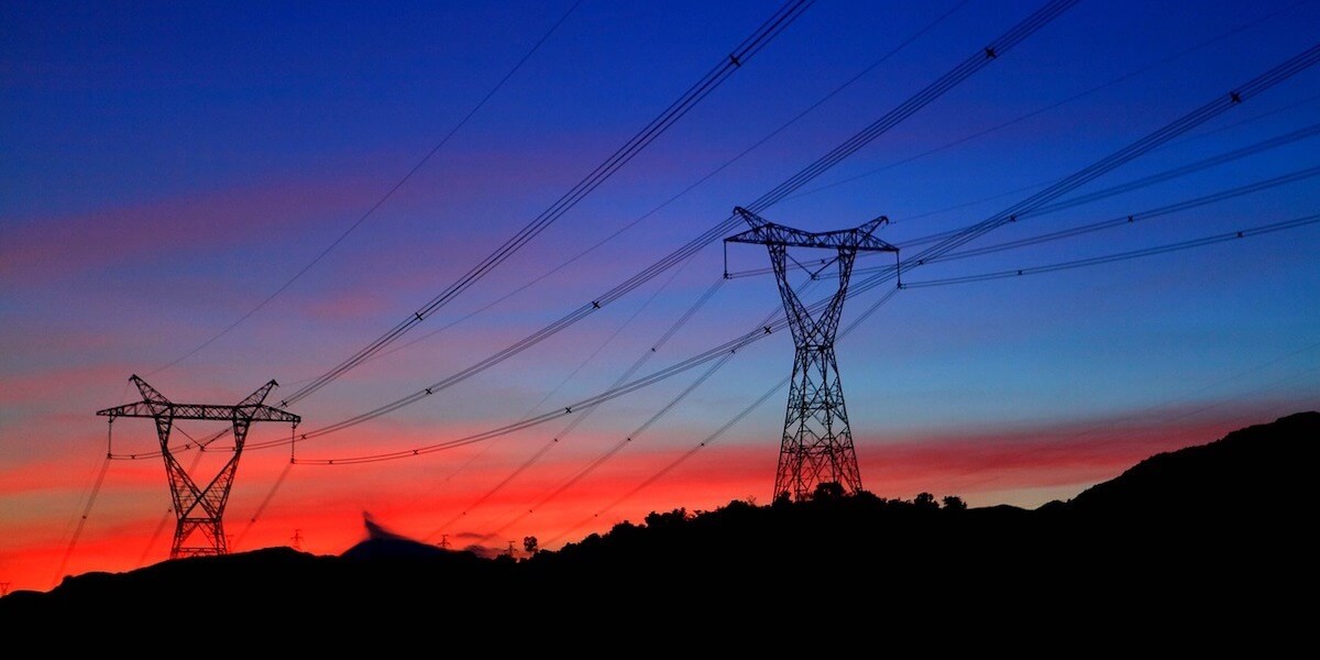 electricity pylons against a backdrop of a sunset with blue and red hues