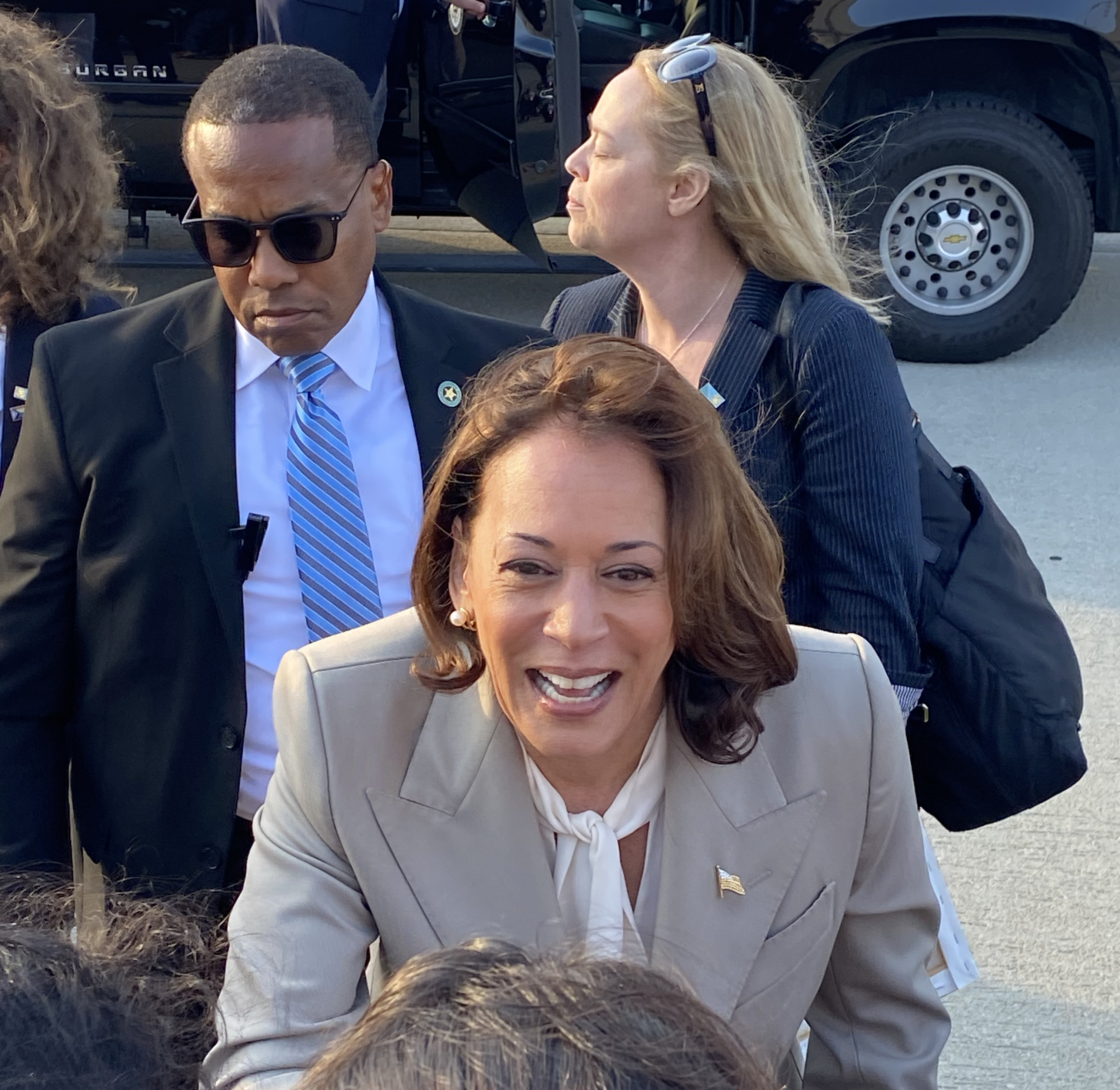 Kamala Harris, wearing a grey coat, outdoors shaking the hand of another person