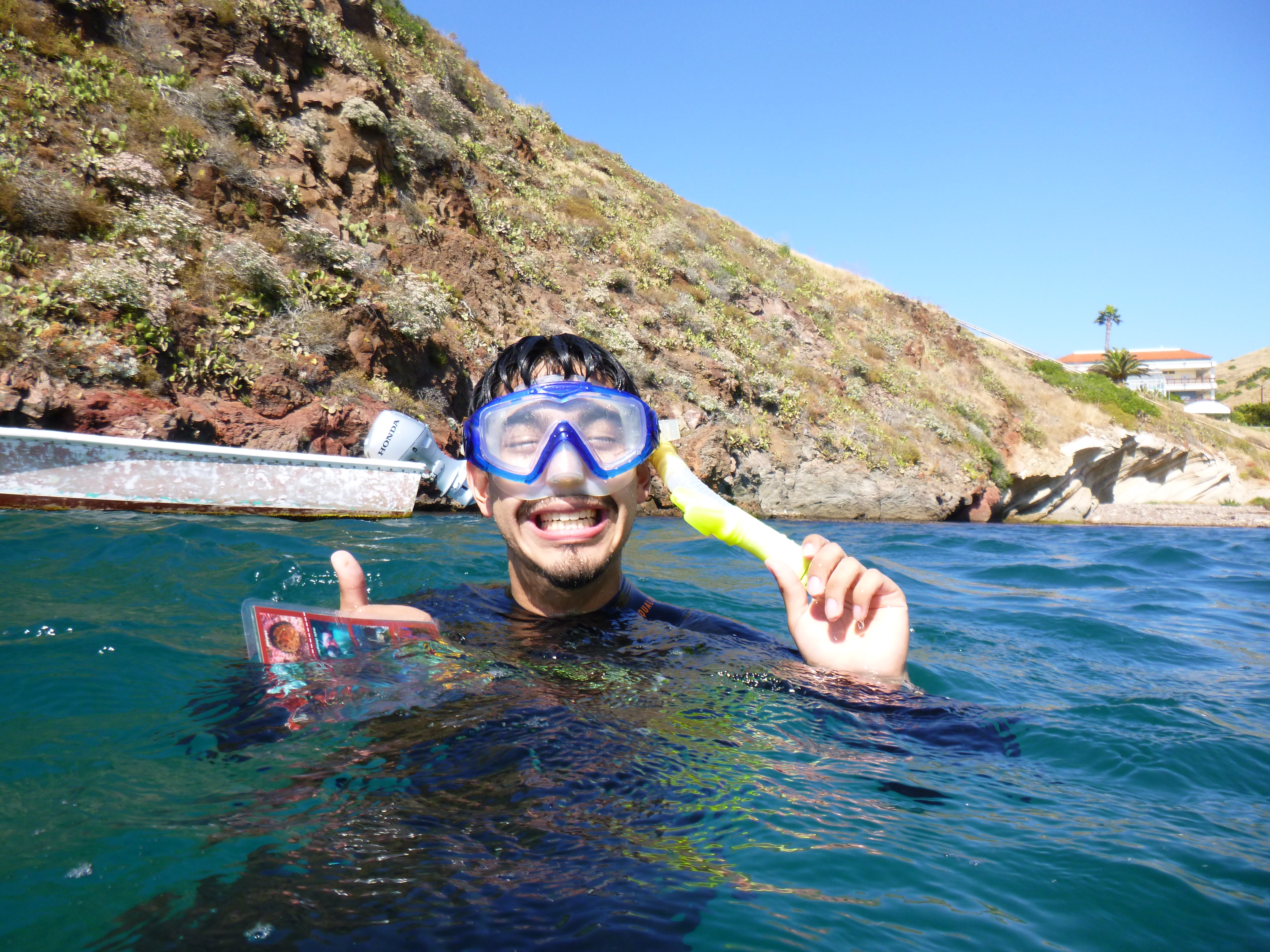 diver in the waters of Big Fisherman Cove grins with one hand holding their snorkel and other giving a thumbs up