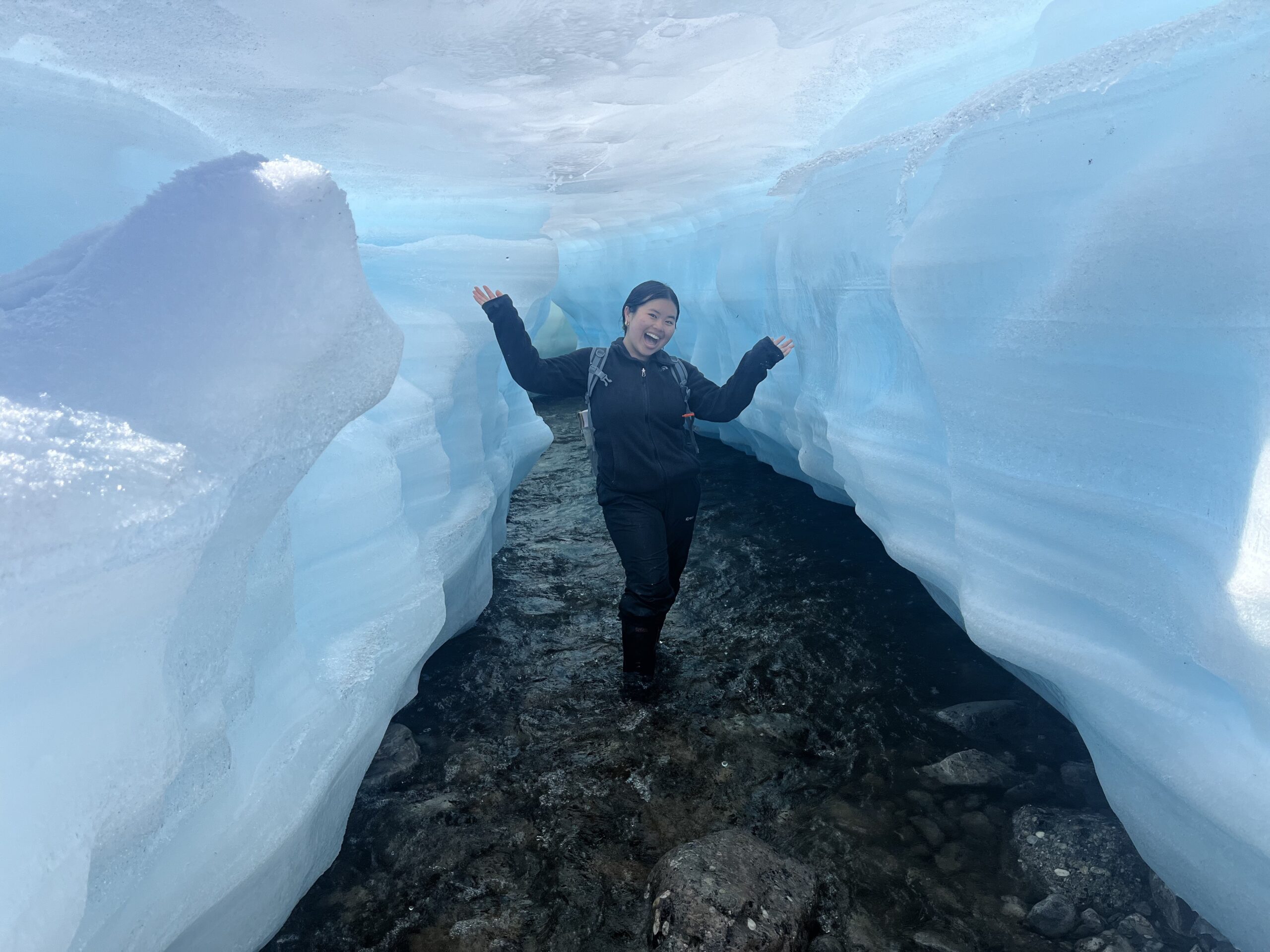 a person stands with their arms up cheerfully in the middle of an icy cavern