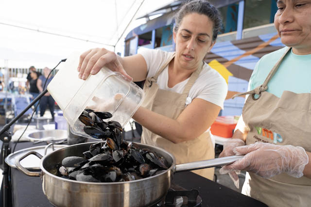 two people in aprons cooking mussels in a pot