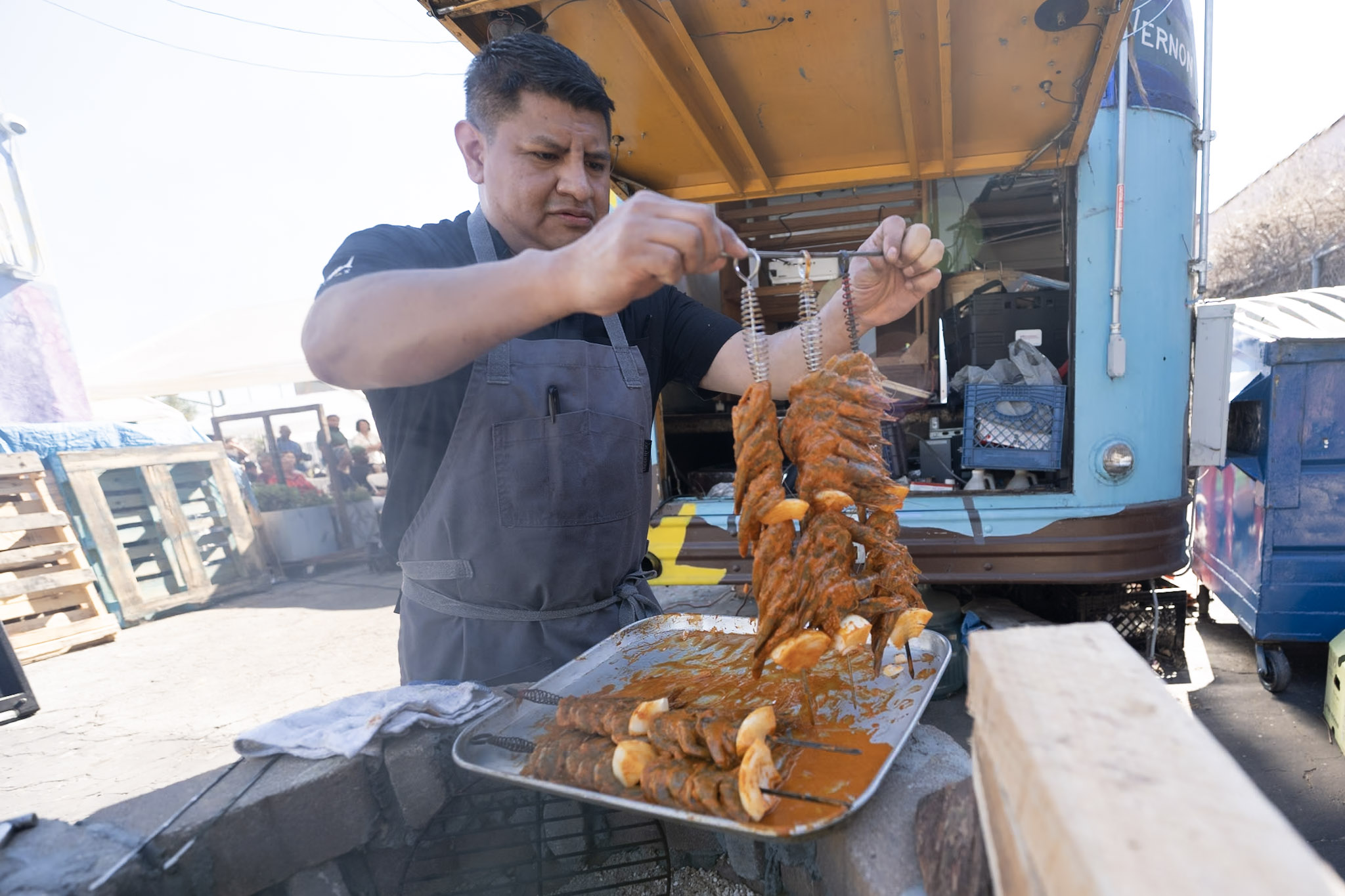 a person wearing in an apron prepares skewered shrimps on a tray