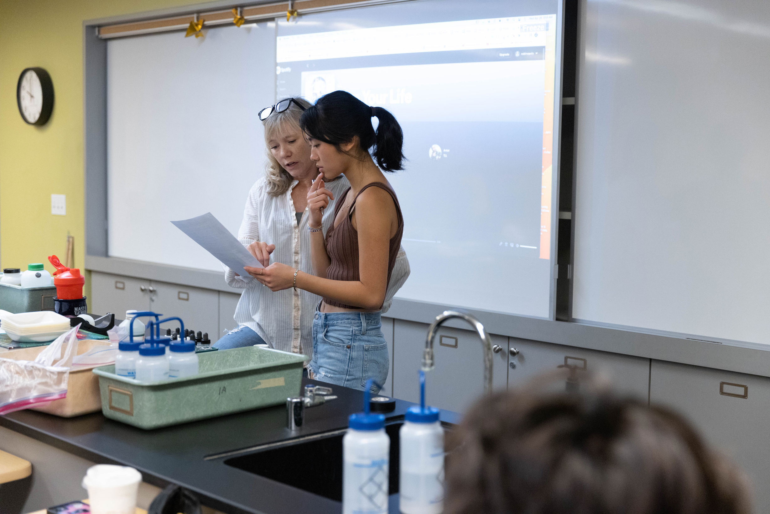 a student and teacher look at an assignment paper together in a chemistry classroom